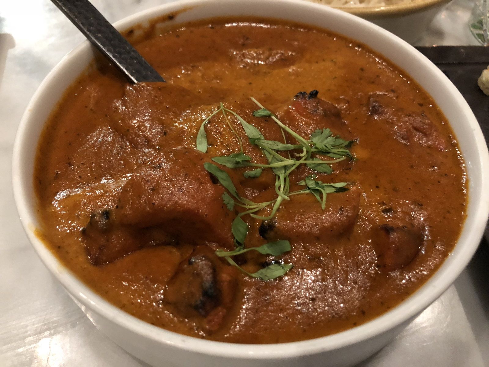 A bowl of butter chicken finished with a swirl of cream and coriander
