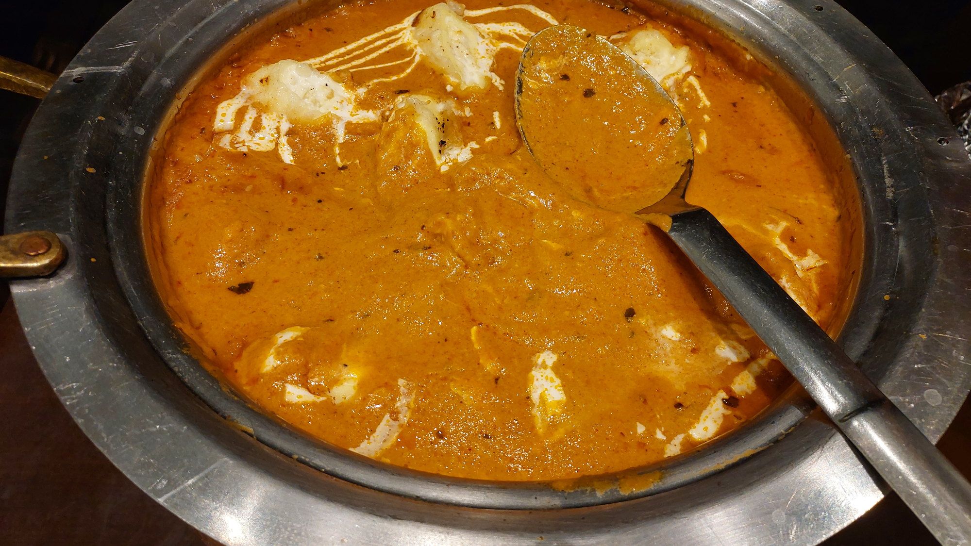 A pan of paneer cubes finishing in a glossy tomato and butter gravy