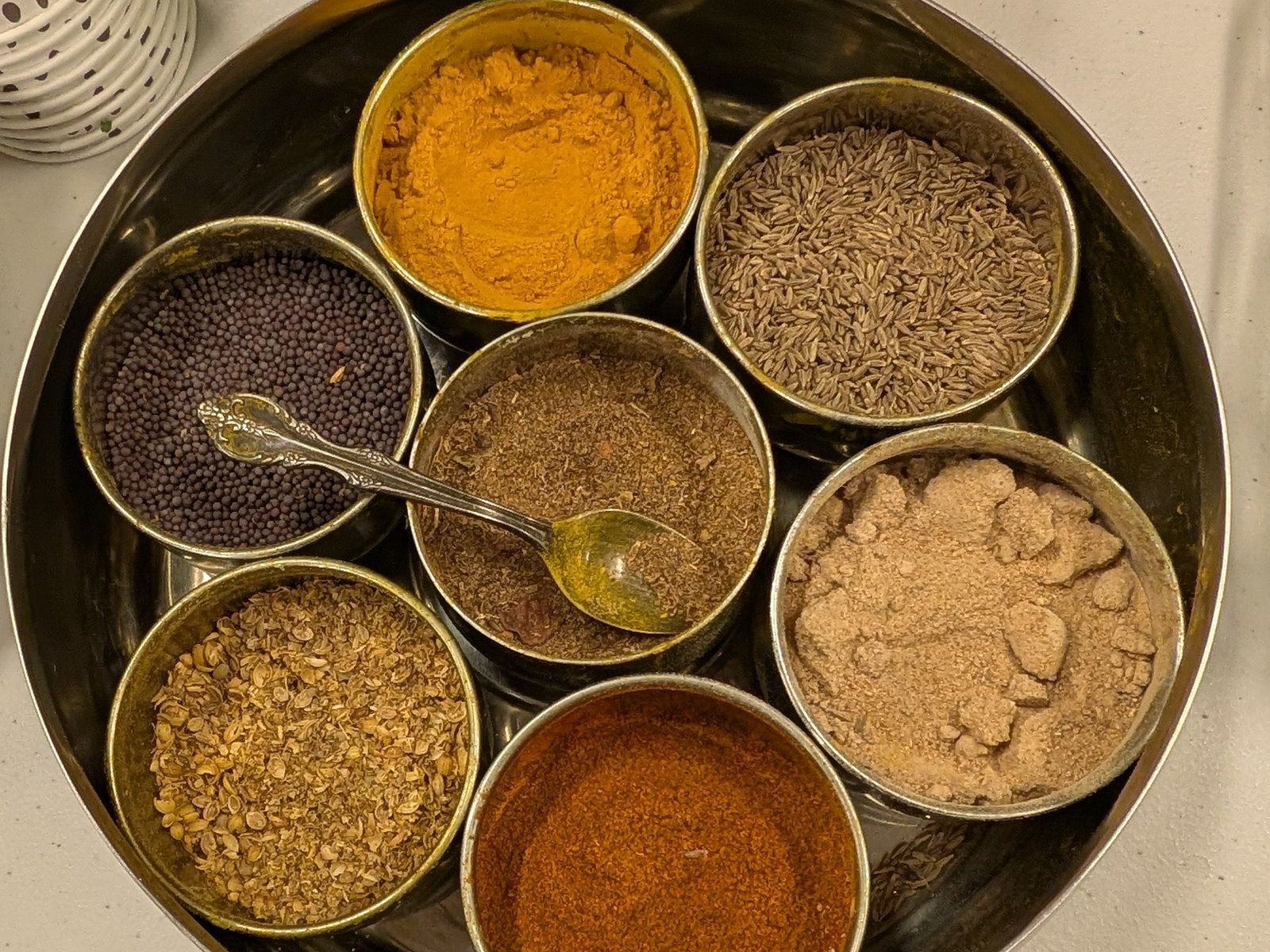 A round steel spice tin, its seven wells filled with ground spice