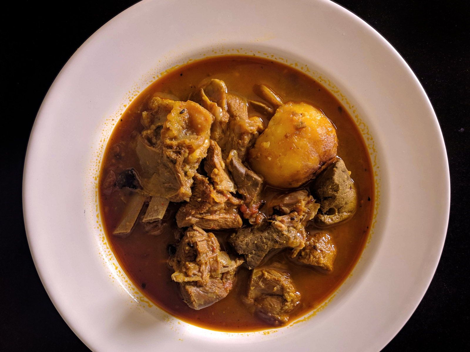 Goat curry with whole spices, shot close on a dark surface