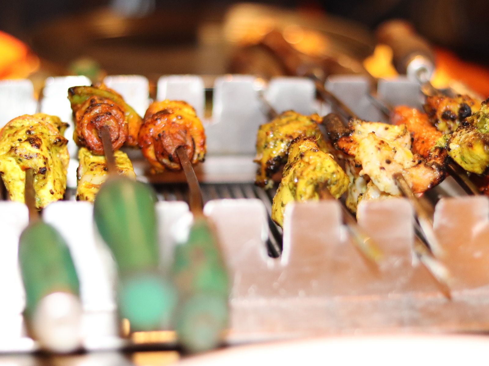 Charred paneer, pepper and onion threaded onto skewers on a white tray