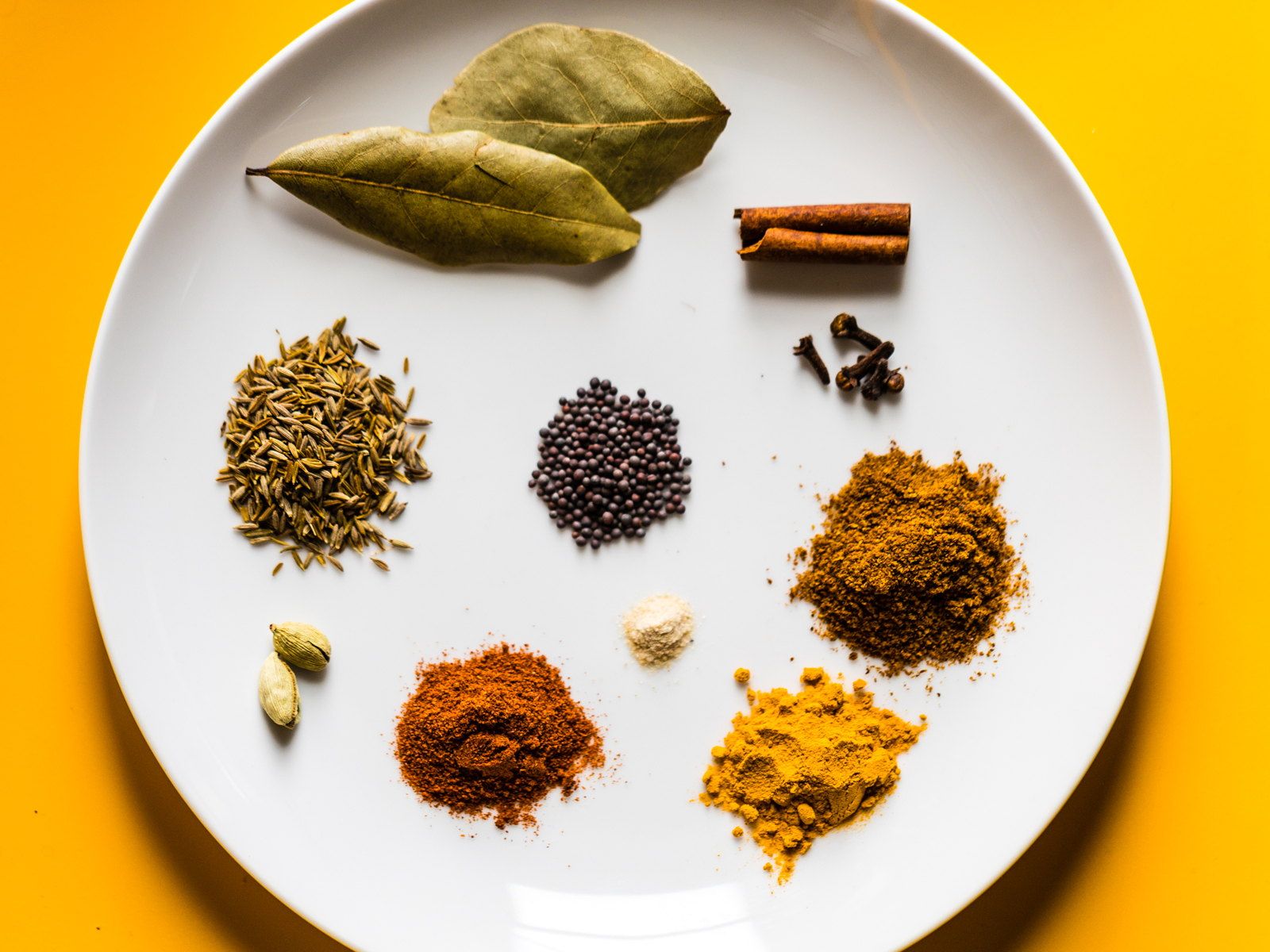 Whole spices — bay, cinnamon, cardamom and turmeric — laid out on a plate