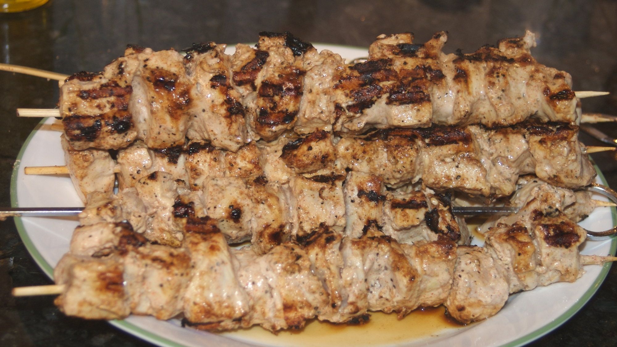 Chicken skewers turning over live coals, edges just catching colour
